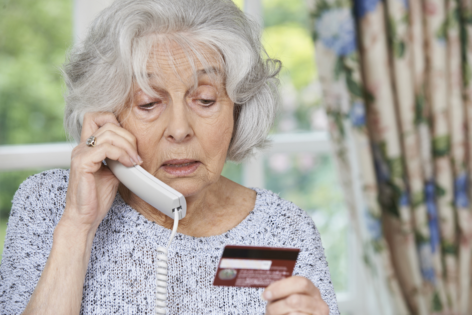 photo of concerned older woman on the phone holding a credit card